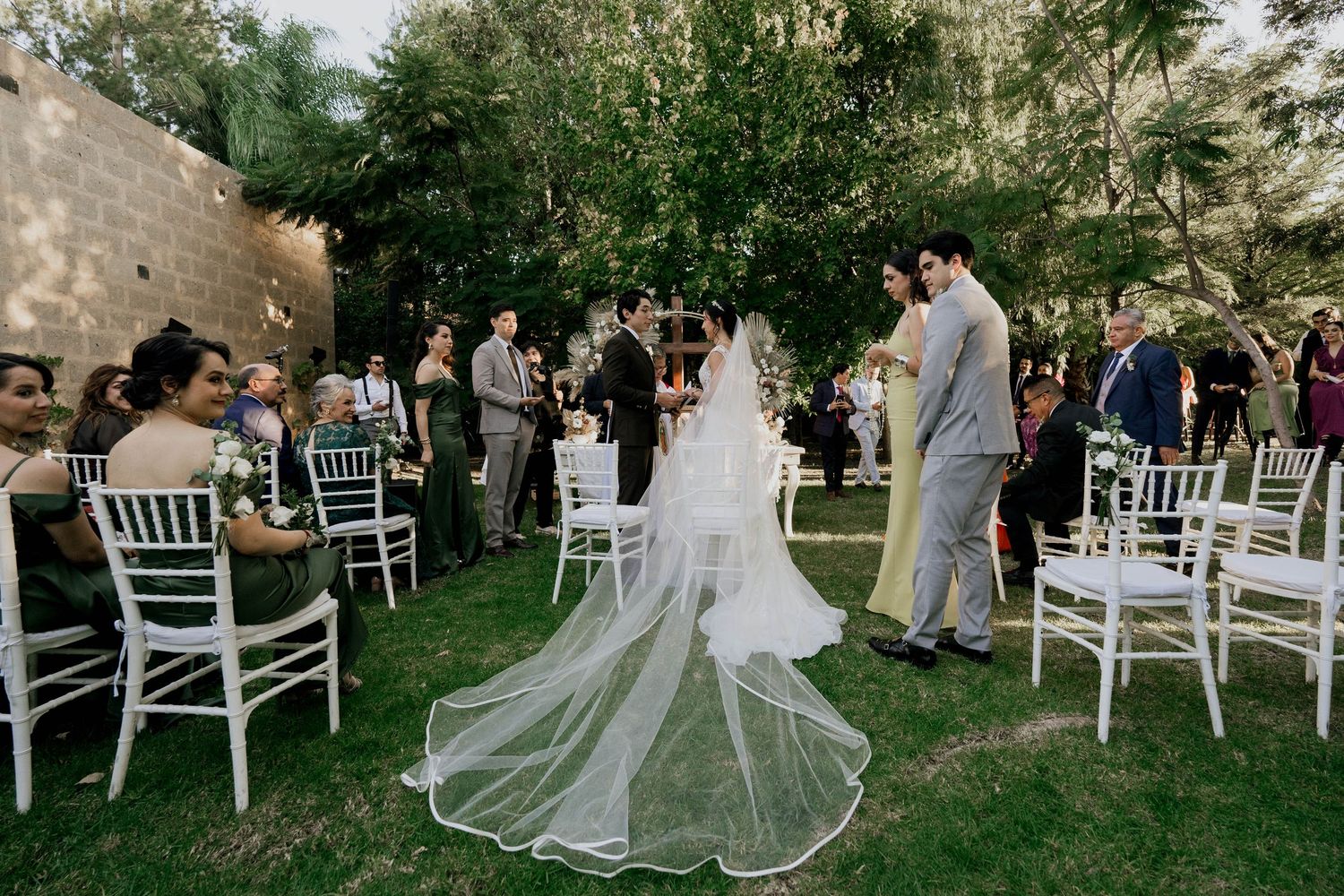 Outdoor wedding ceremony setup with white chairs arranged on a grassy lawn under trees at dusk.
