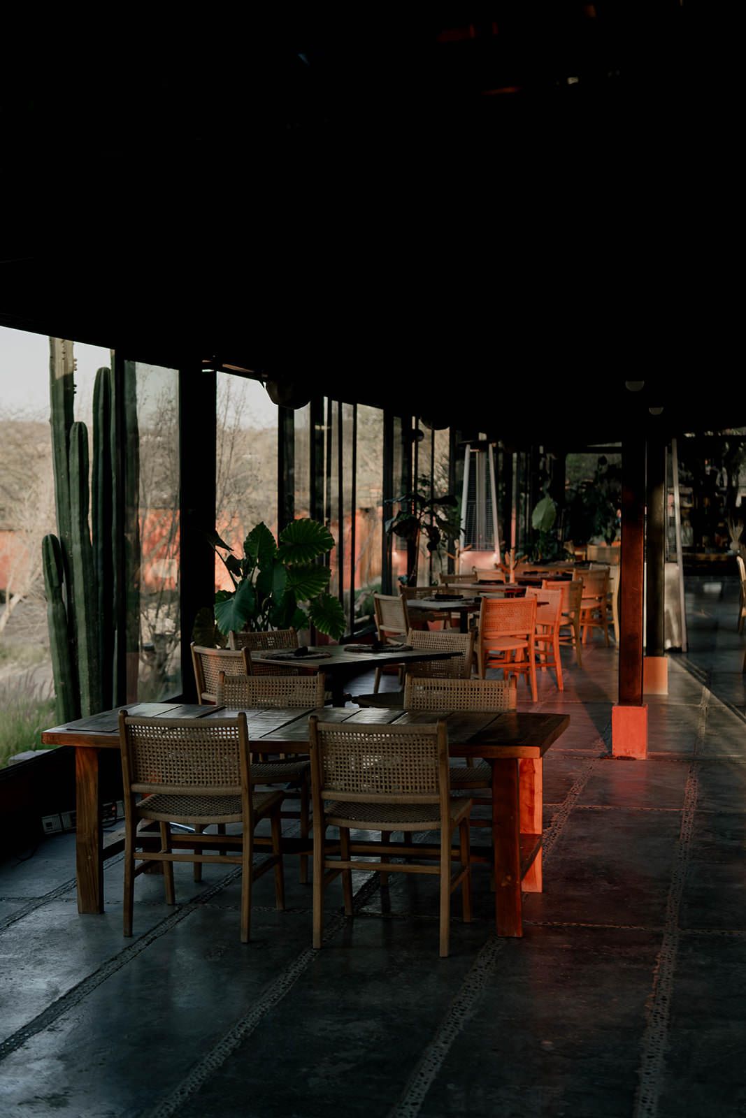 Empty rustic restaurant interior with wooden tables and chairs in warm lighting.