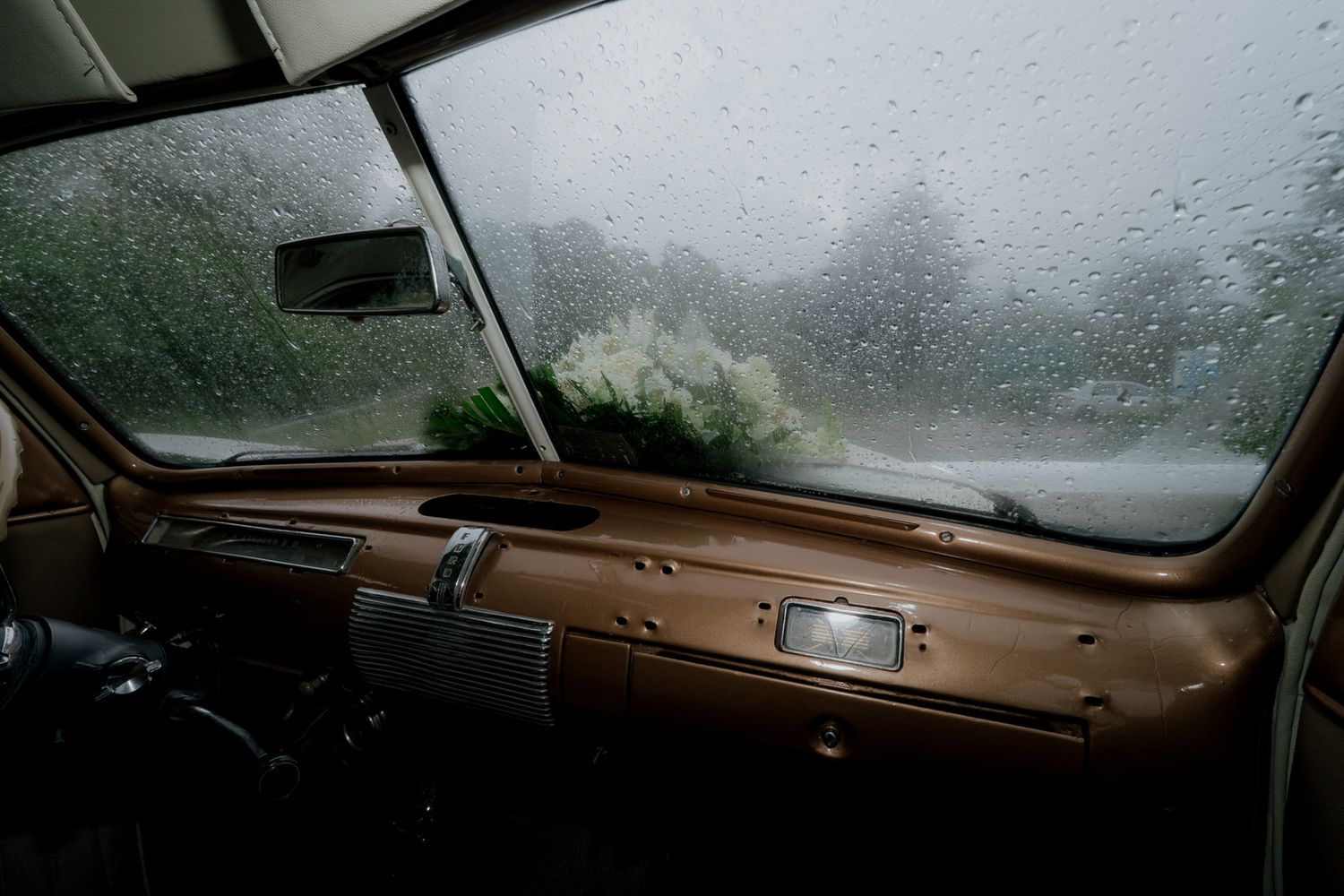 Raindrops on vintage car windshield creating a moody atmosphere.