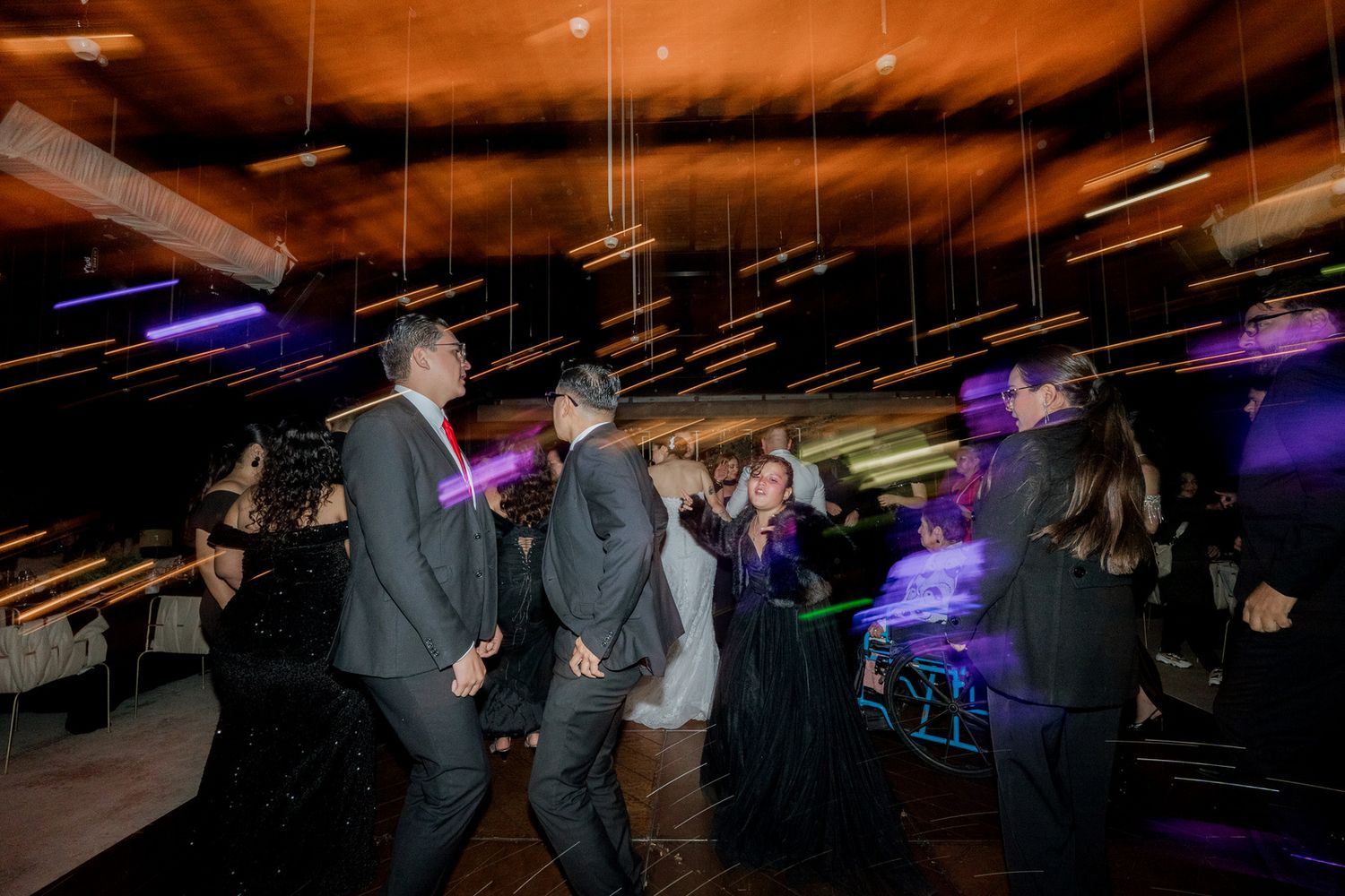 Wedding party dancing under dramatic purple lighting at an indoor reception venue.