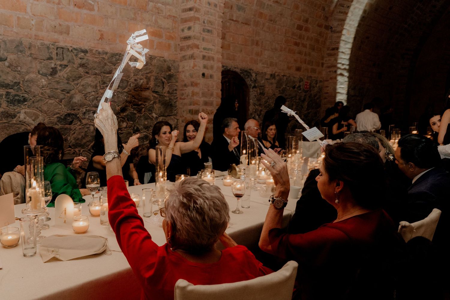 Guests dancing and celebrating at a dimly lit indoor wedding reception with brick walls.
