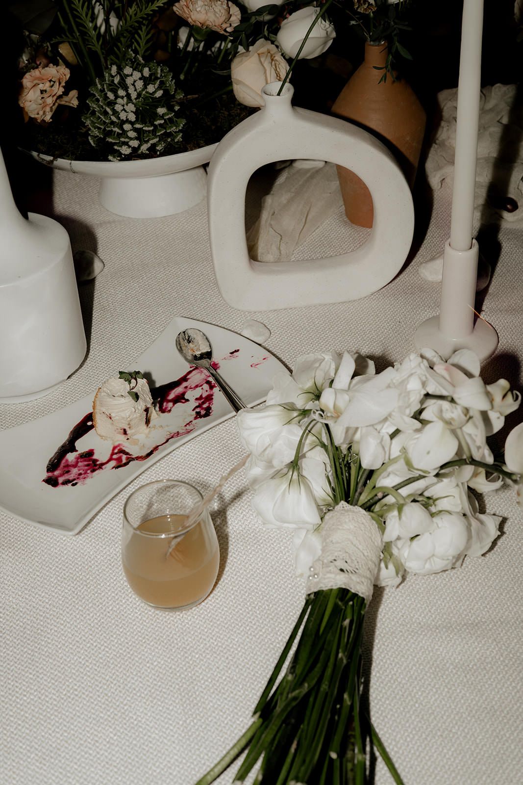Wedding table detail with white ranunculus bouquet, cake slice, and candle decor.