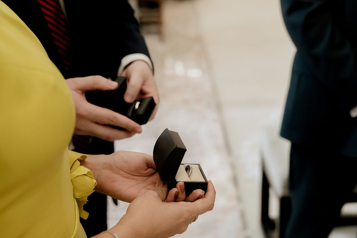 Close-up of wedding rings in black velvet boxes held by guests during a church wedding ceremony.