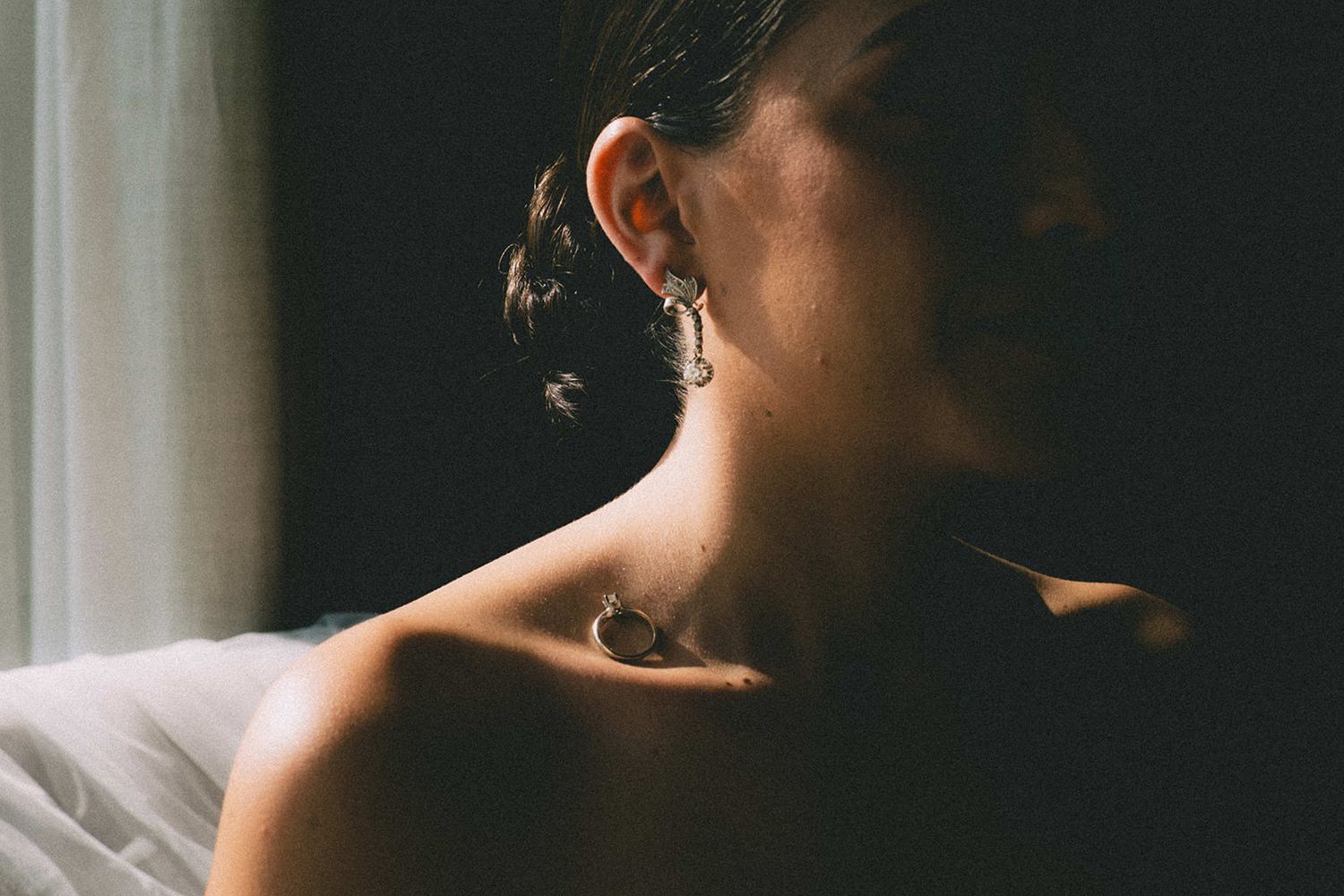Close-up of bride with elegant updo, earring, and small neck tattoo in soft window light.