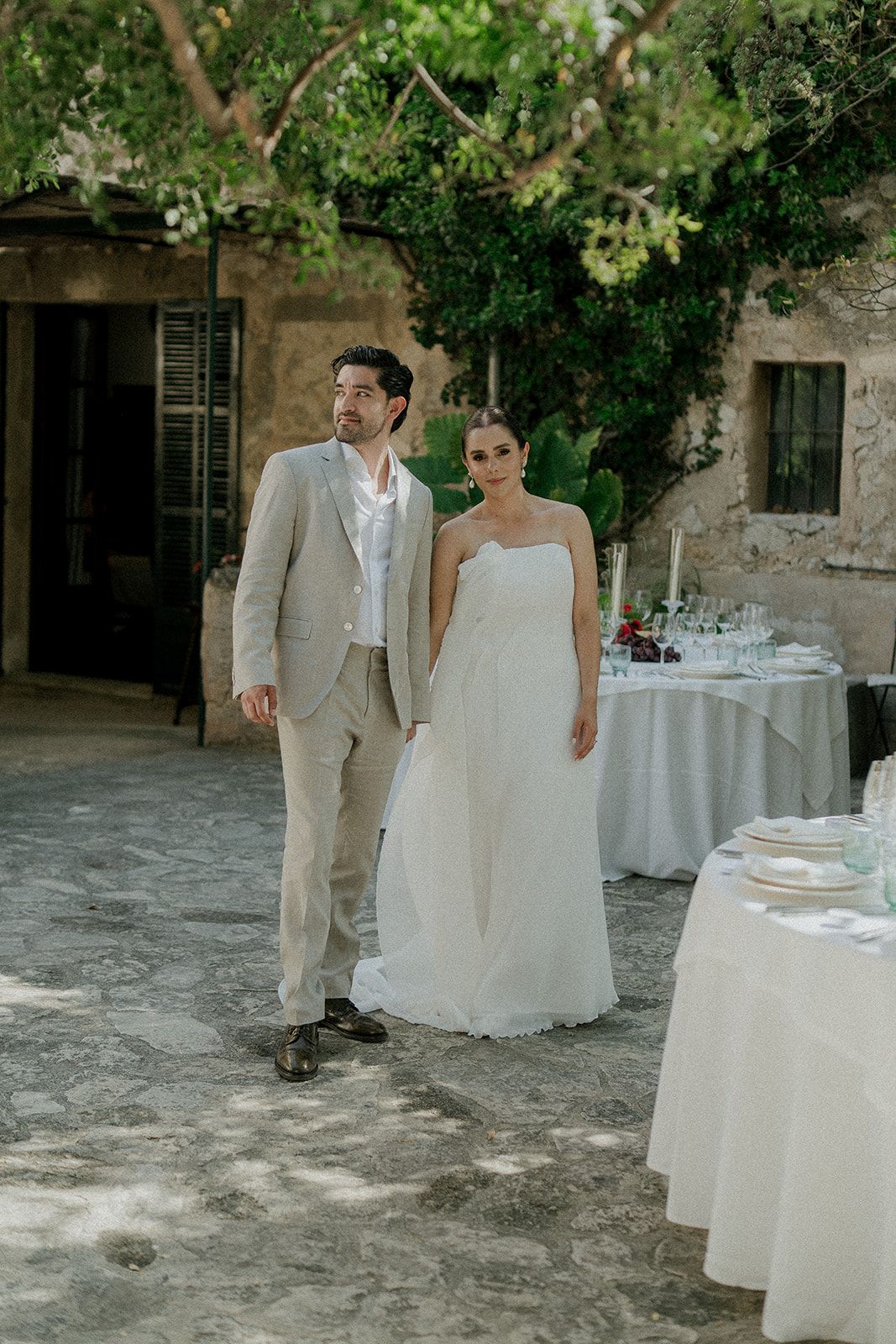 Elegant outdoor wedding reception setup with white tablecloths and lush green garden backdrop.