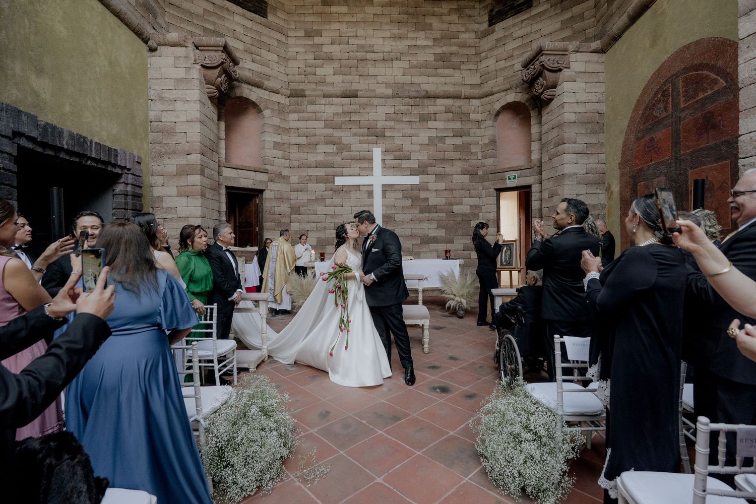 Wedding ceremony setup in a historic brick courtyard with white chairs and greenery decorations.