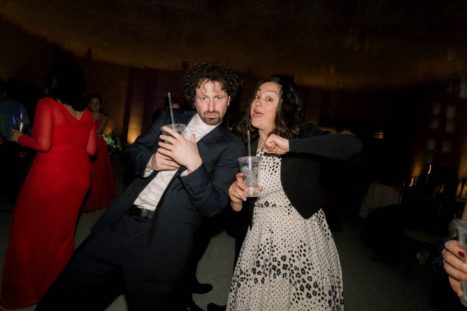 Party guests dancing and socializing in a dark reception venue.