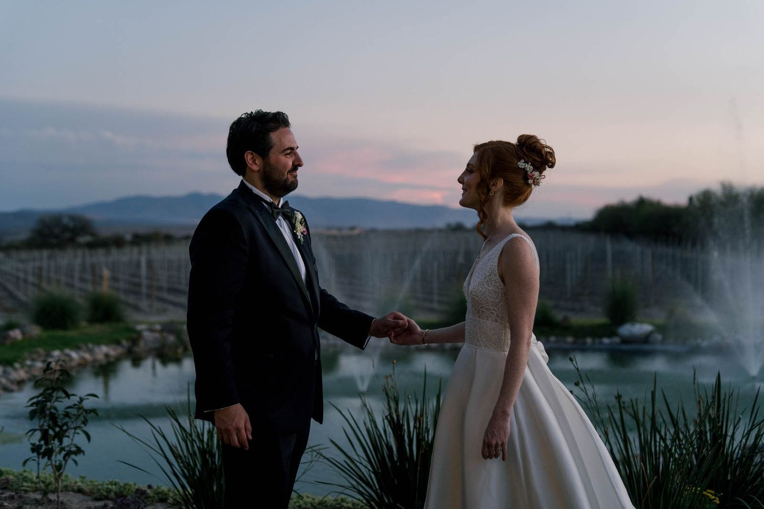 A couple shares an intimate moment at twilight beside a water feature and mountain landscape.