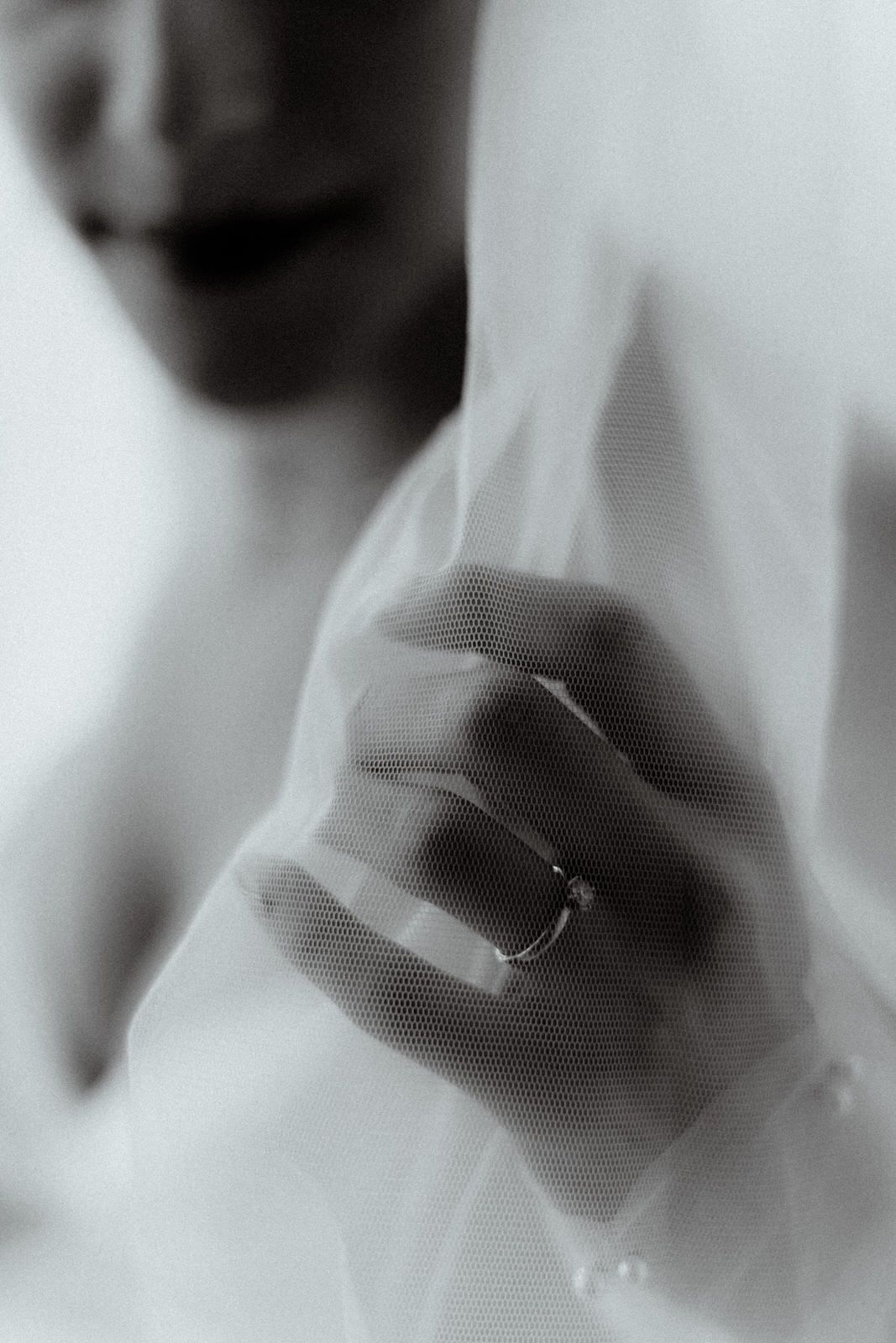 Ethereal black and white close-up of a wedding ring through delicate veil fabric.