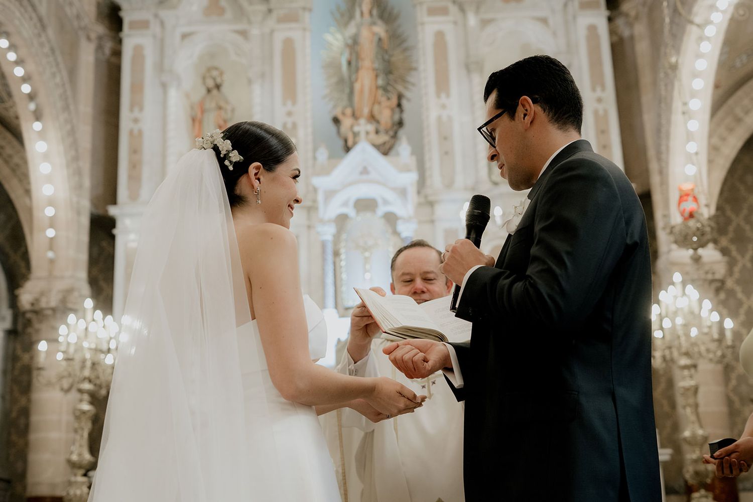 Bride and groom exchanging rings with ring bearer child in ornate church wedding ceremony.