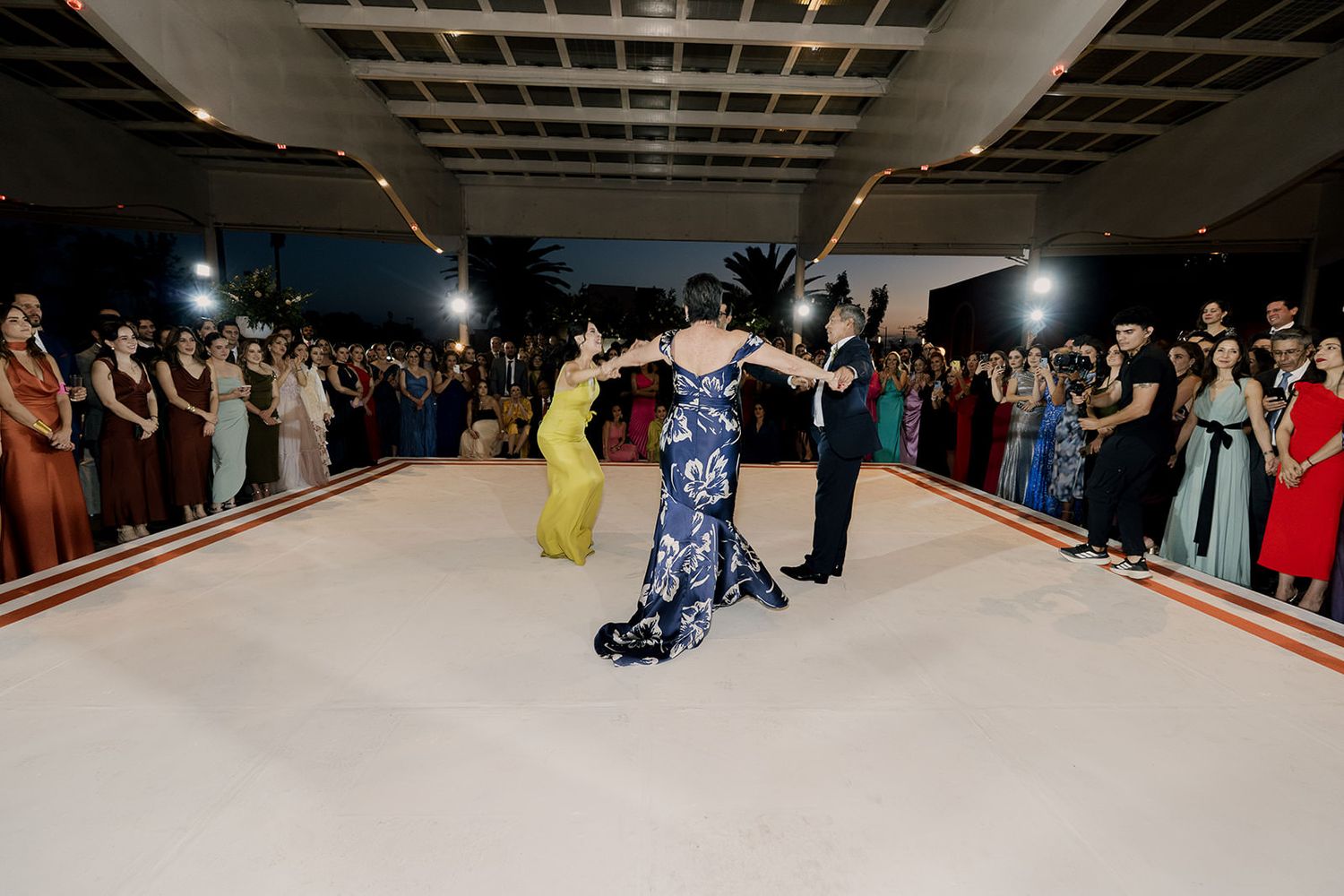 Bride and groom share a dramatic first dance surrounded by cheering guests at a wedding reception.