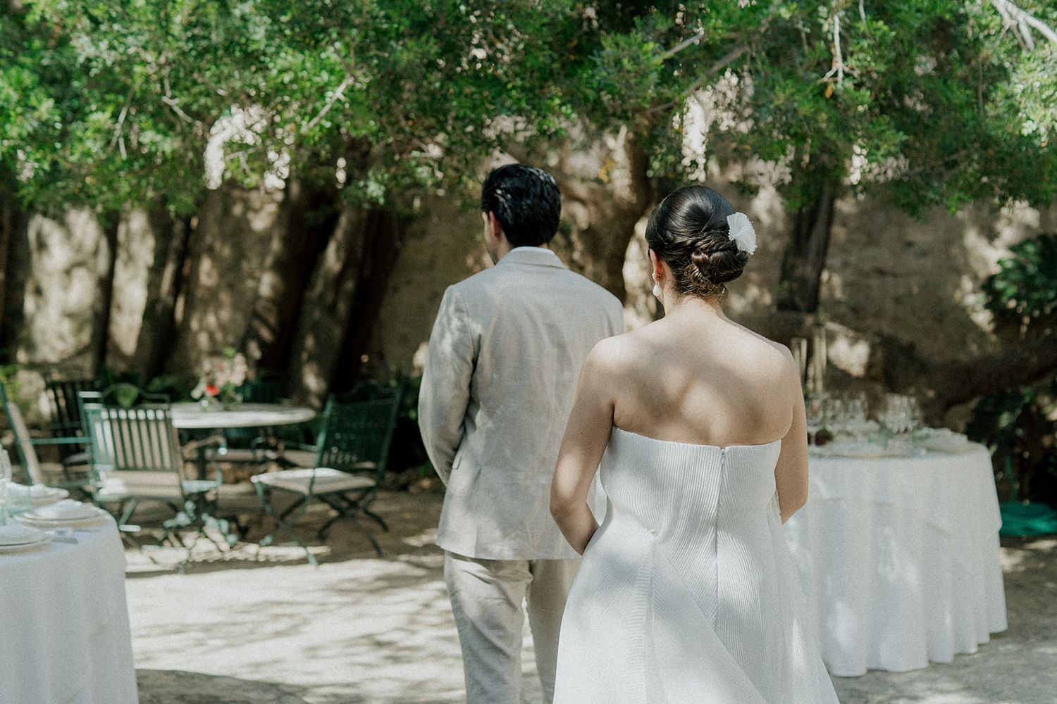 Wedding ceremony space arranged outdoors with white chairs and natural greenery backdrop.