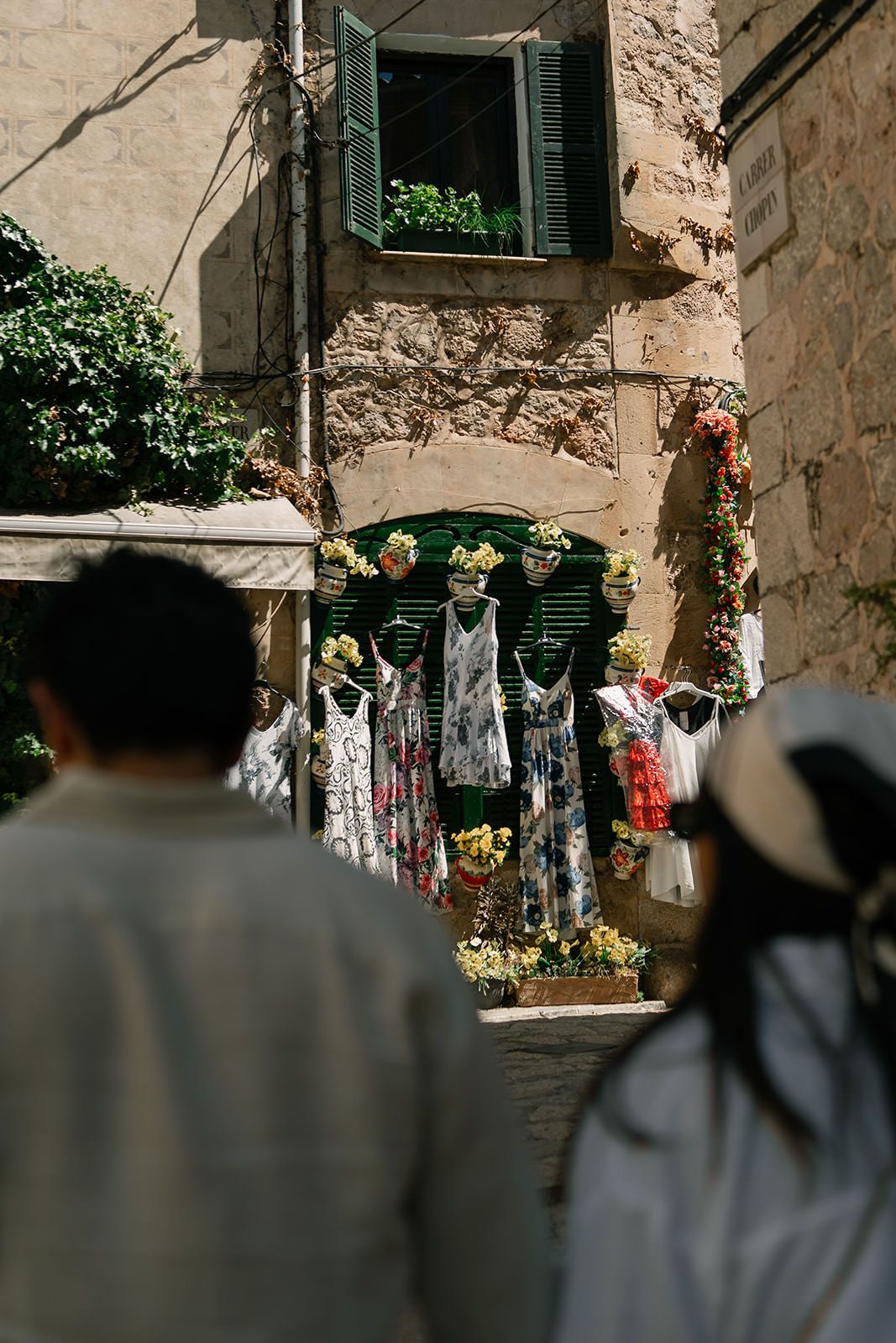 Clothes hanging on lines against stone walls in a Mediterranean street scene with sunlight and shadows.