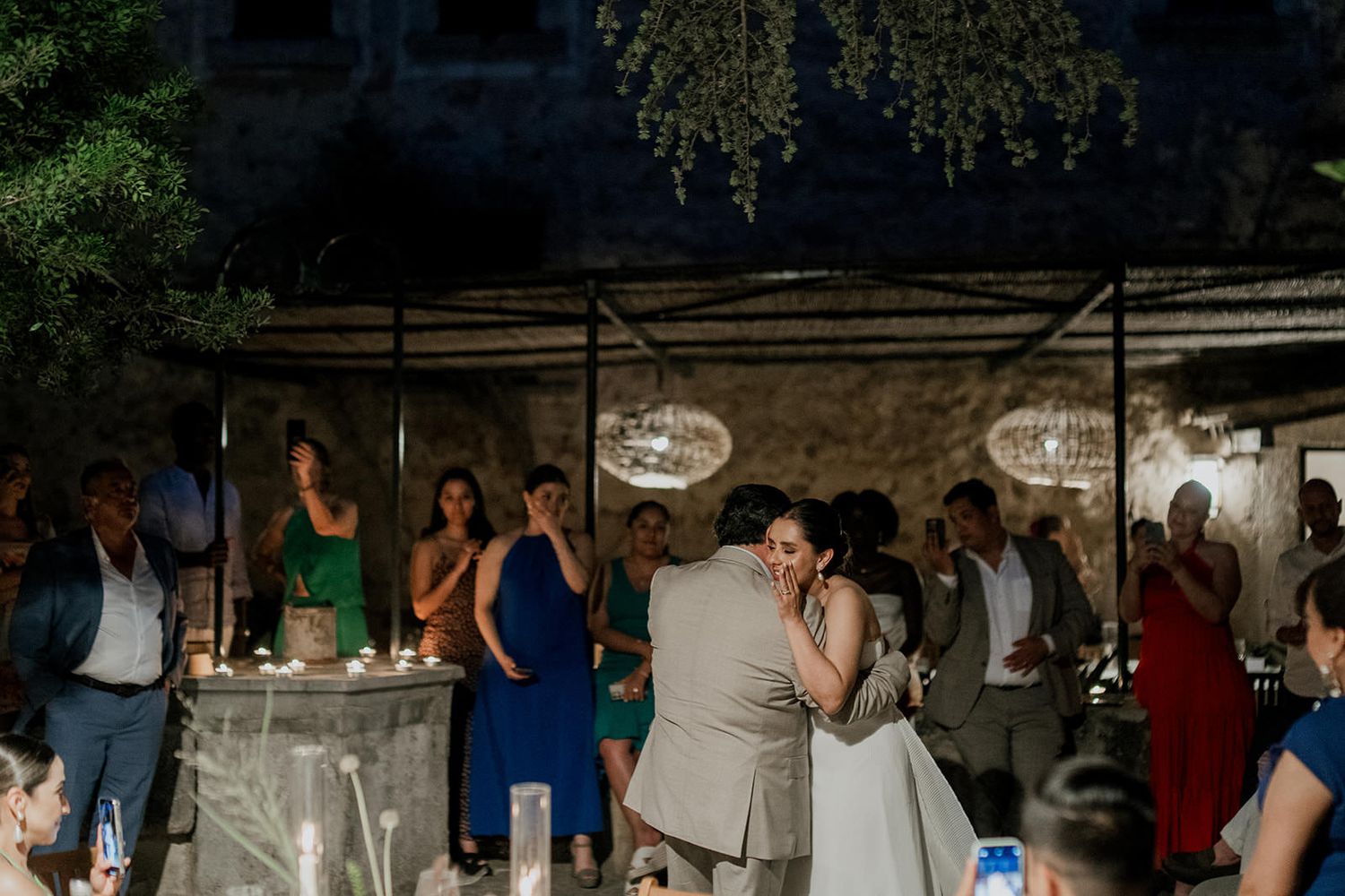 Guests dancing and celebrating at a lively wedding reception under string lights and rustic decor.