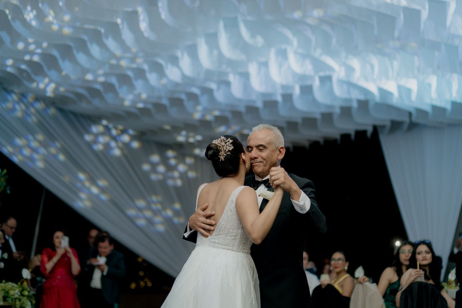 Couple shares romantic first dance under decorative white ruffled ceiling installation at wedding.