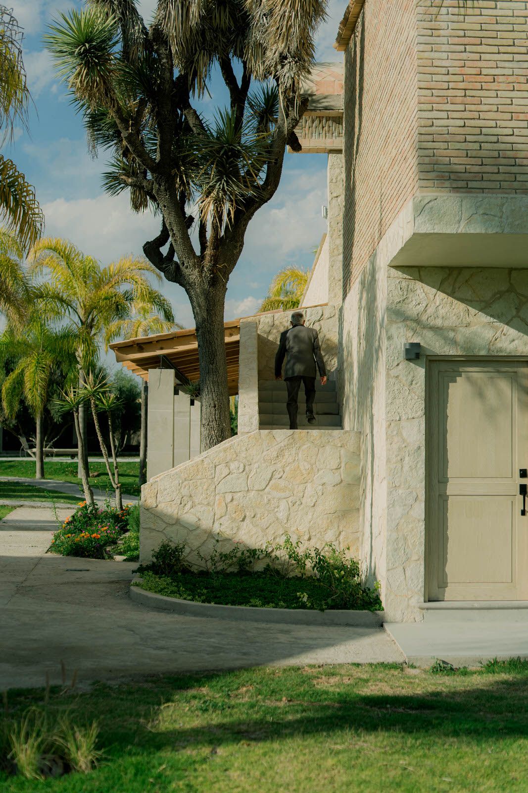 Modern white stone building exterior with palm trees and landscaping under blue sky.