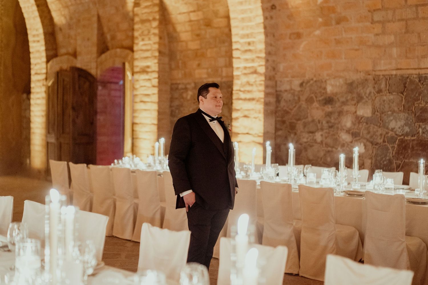 Elegant wedding reception setup in a vaulted brick cellar with white-covered chairs.