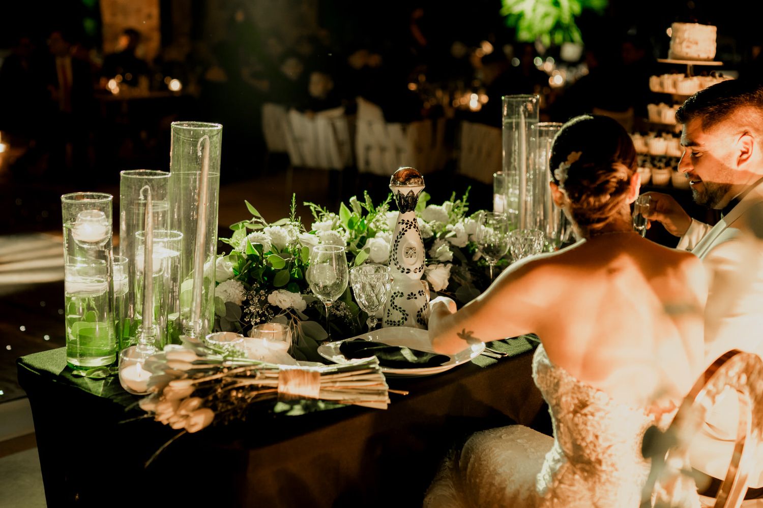 Wedding reception table settings with glowing candles and greenery decorations.