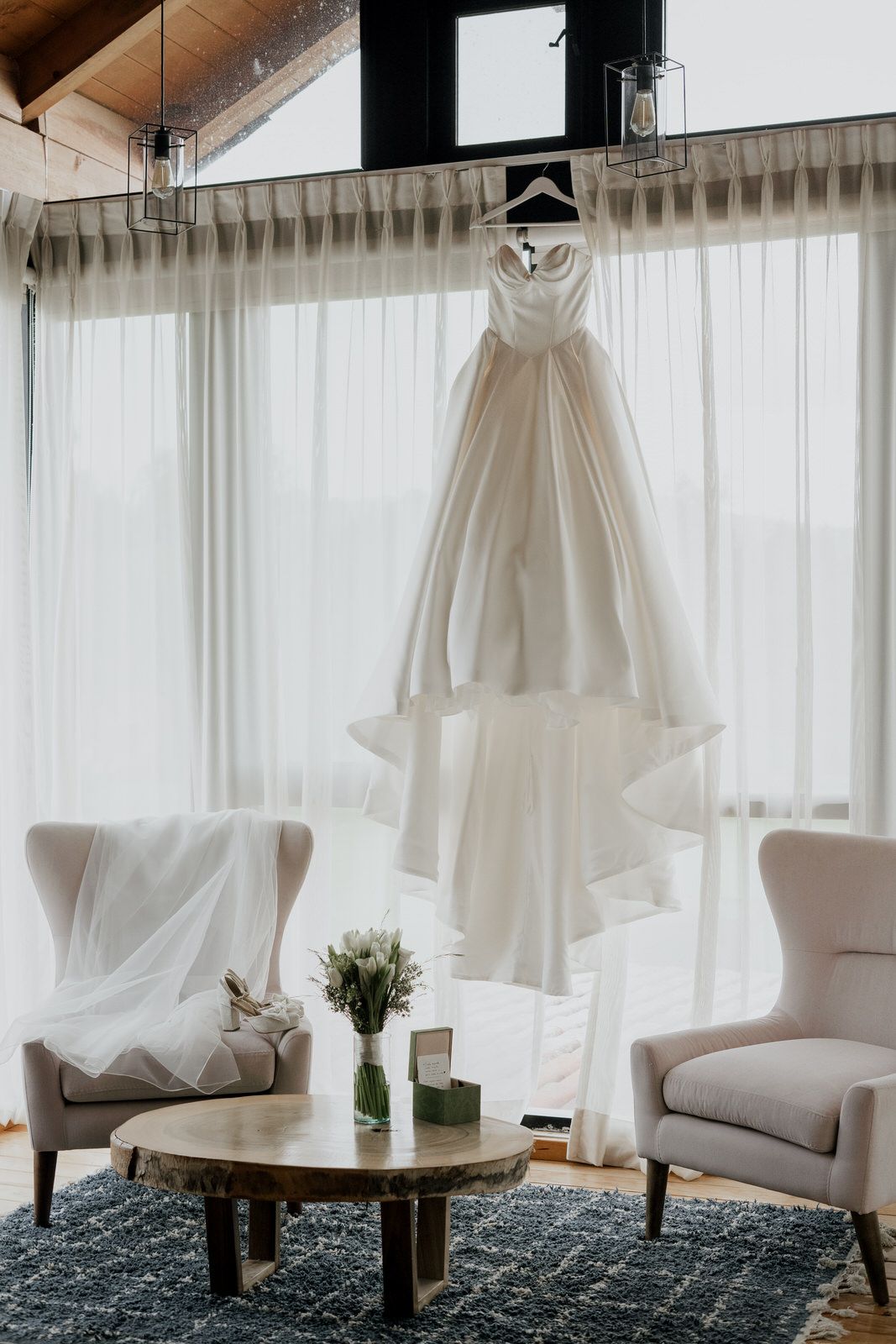 Elegant bridal preparation room with white dress displayed near window and comfortable seating area.