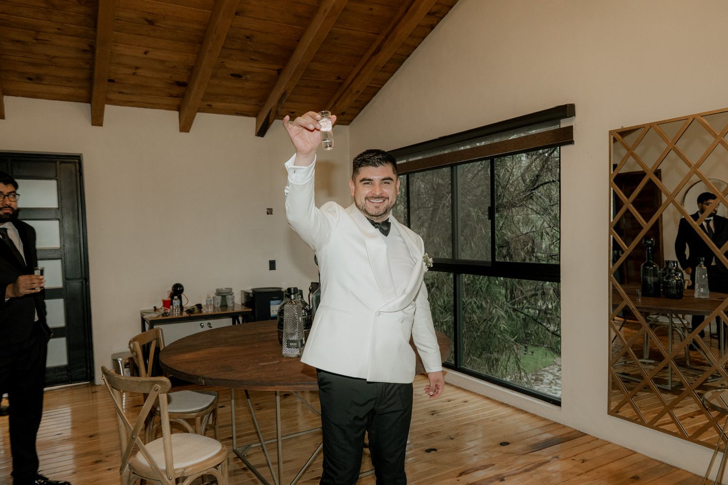 Person in white dress shirt raises arm in celebration inside modern room with wooden beams and large windows.