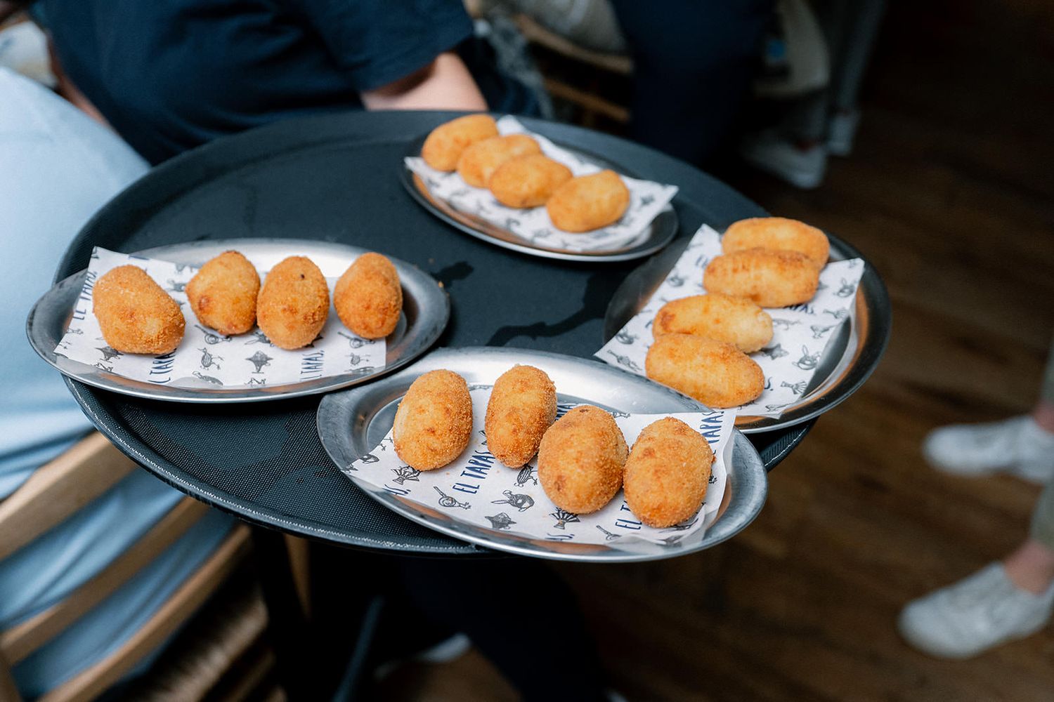 Multiple plates of golden-brown croquettes or breaded appetizers arranged on dark plates against a wooden surface.