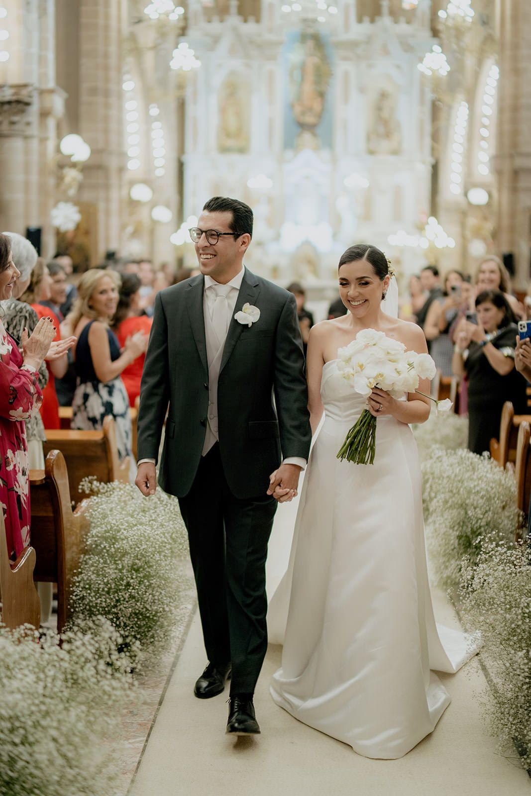 A smiling bride and groom walk hand in hand down the aisle after their church wedding ceremony.