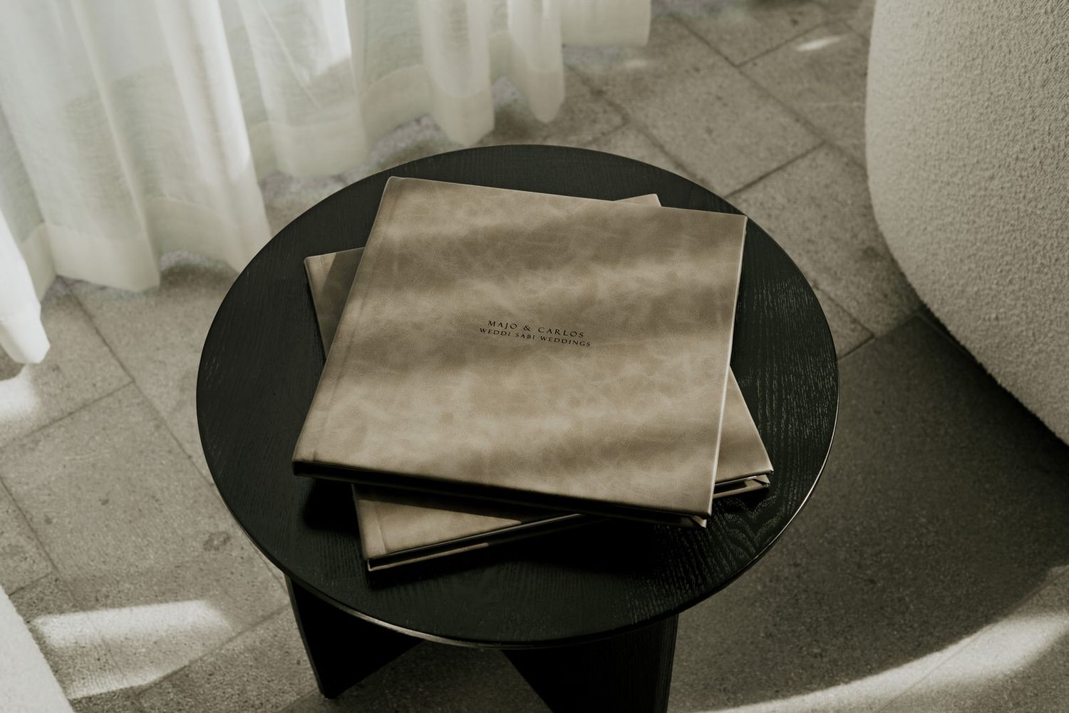 Two beige leather-bound menus stacked on a round black side table near a white curtain.