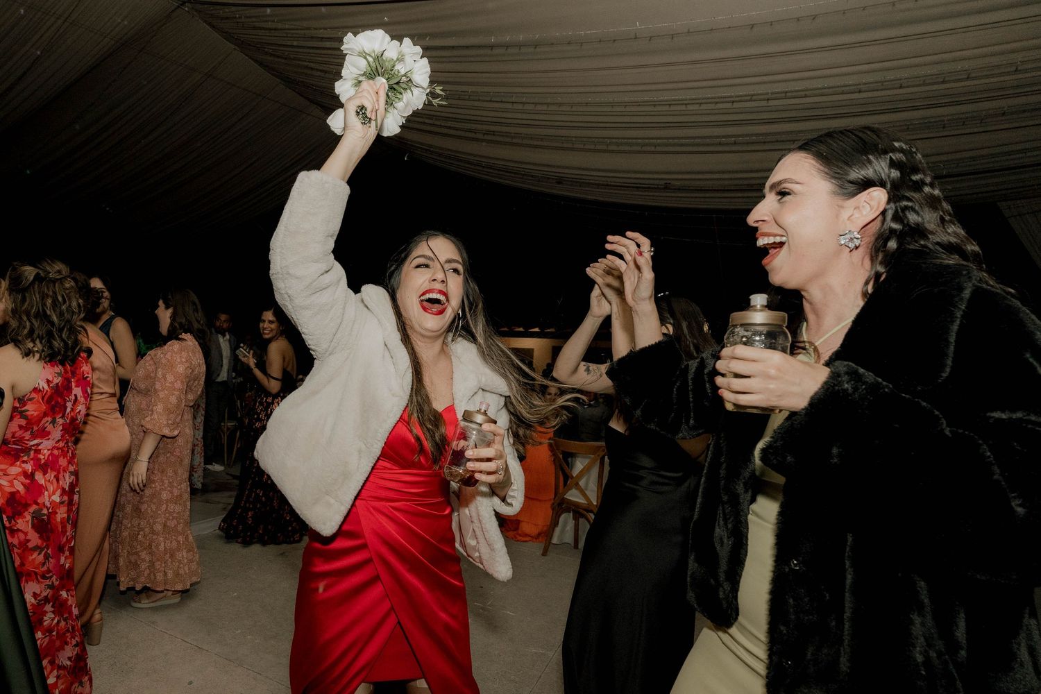 Wedding reception guests dancing and celebrating under dimly lit draped ceiling.
