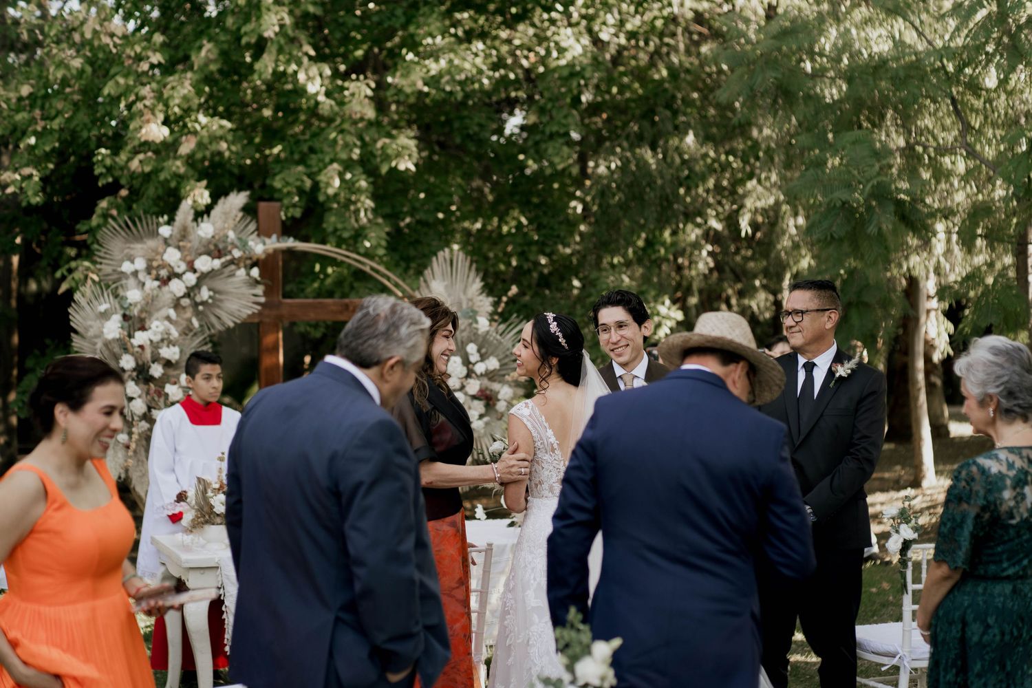 Wedding guests gather outdoors under trees for a celebration ceremony.