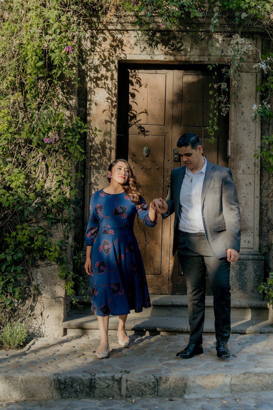 A couple shares a moment by a rustic wooden door framed with climbing vines.