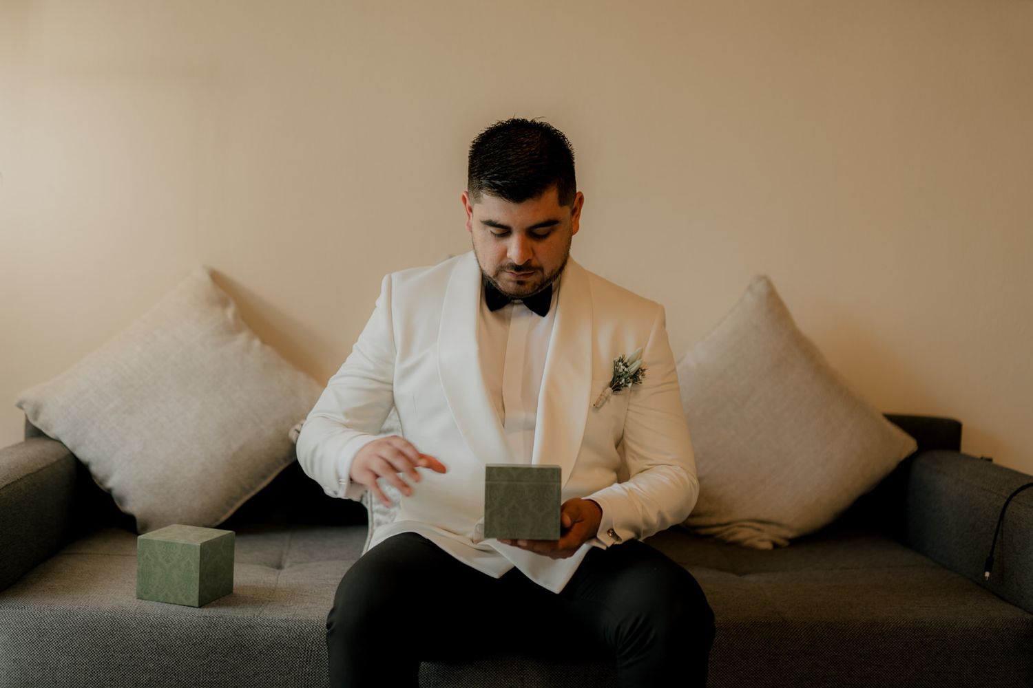 Person in white tuxedo jacket sits on grey couch examining small boxes.