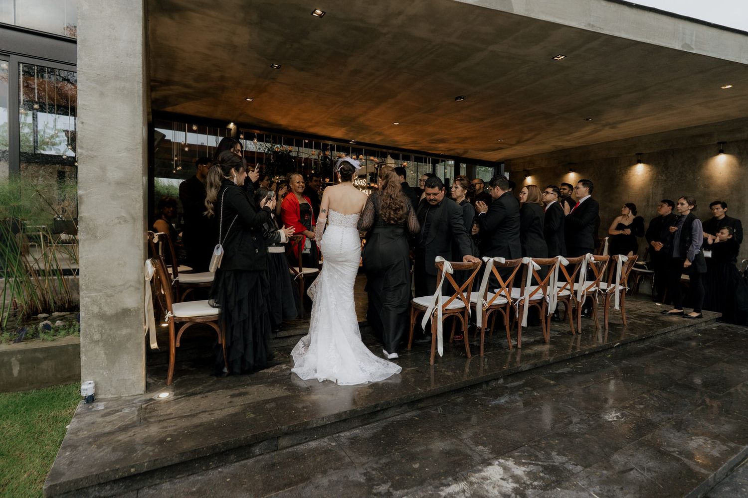 Modern indoor wedding ceremony space with concrete pillars and rows of guest seating.