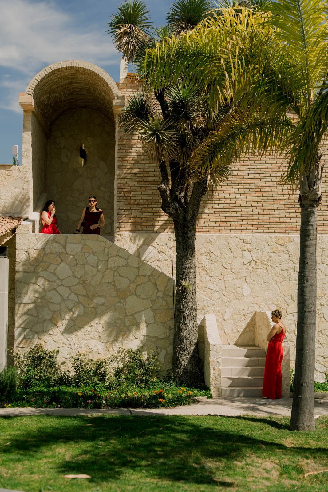 Stone wall courtyard with palm trees and arched doorways under blue sky.