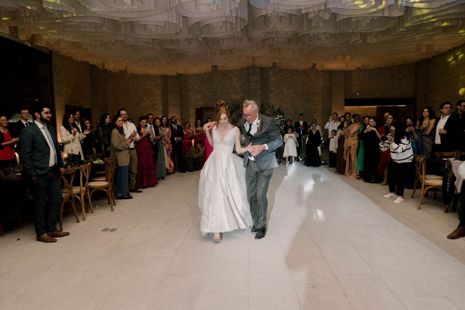 A panoramic view of a wedding reception with guests surrounding an illuminated dance floor.