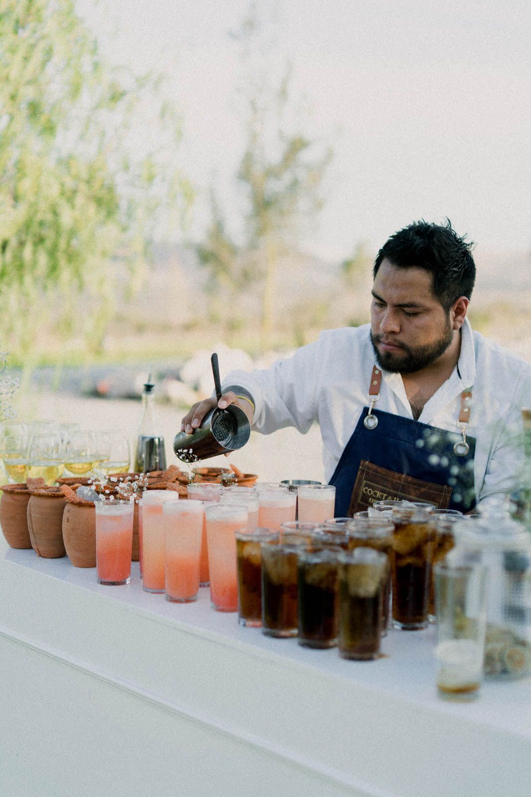 Professional bartenders preparing colorful cocktails at an outdoor bar setup.