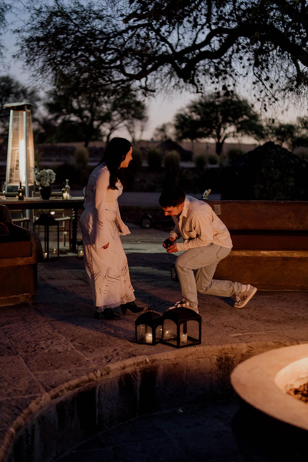 Two figures sit beside glowing lanterns at dusk in a desert setting.