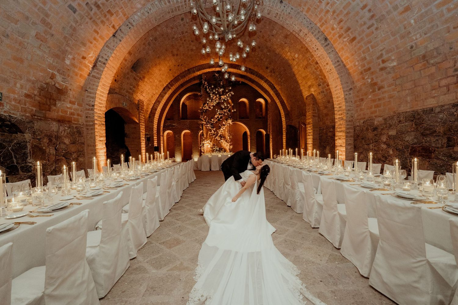 Elegant wedding reception setup in a brick vault with white linens and candlelight.