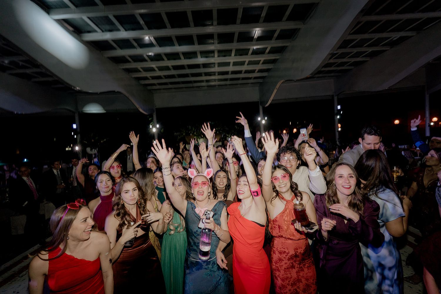 Large crowd of elegantly dressed guests dancing and raising hands at a festive wedding reception party.