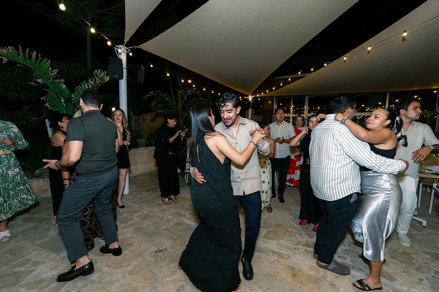 Couples dancing together at a dimly lit evening celebration with string lights overhead.