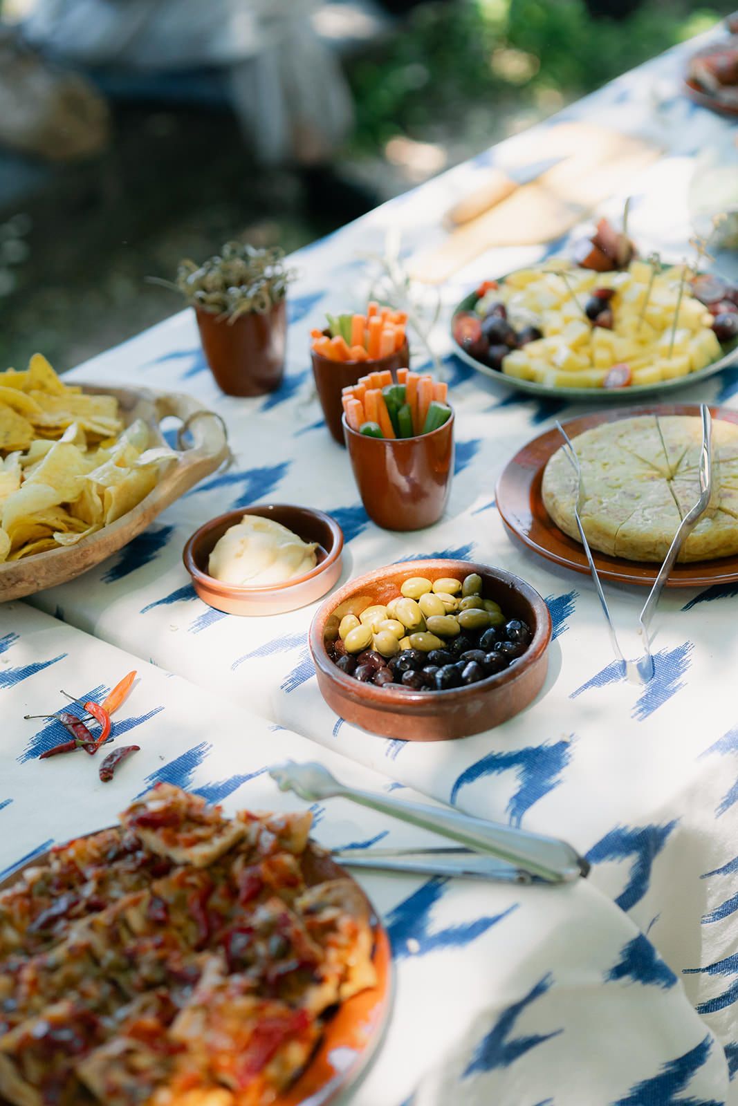 A table spread with Spanish tapas dishes including olives, chips, and various appetizers on a blue and white tablecloth.