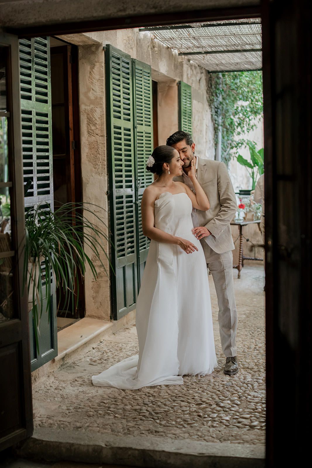 A romantic moment unfolds beneath green shutters in a charming Mediterranean courtyard setting.