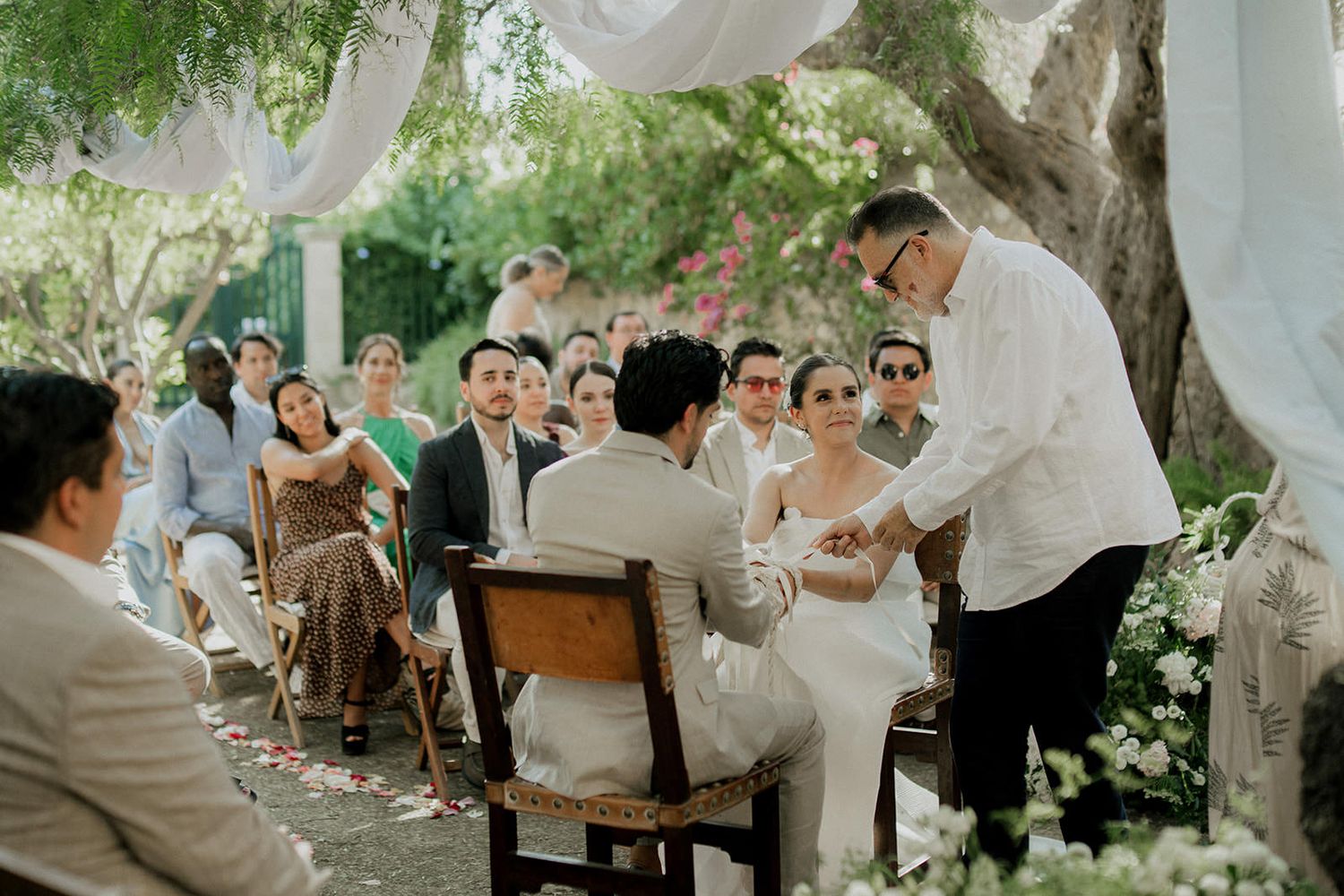 Guests seated at wooden tables during an outdoor garden wedding reception under draped white fabric.