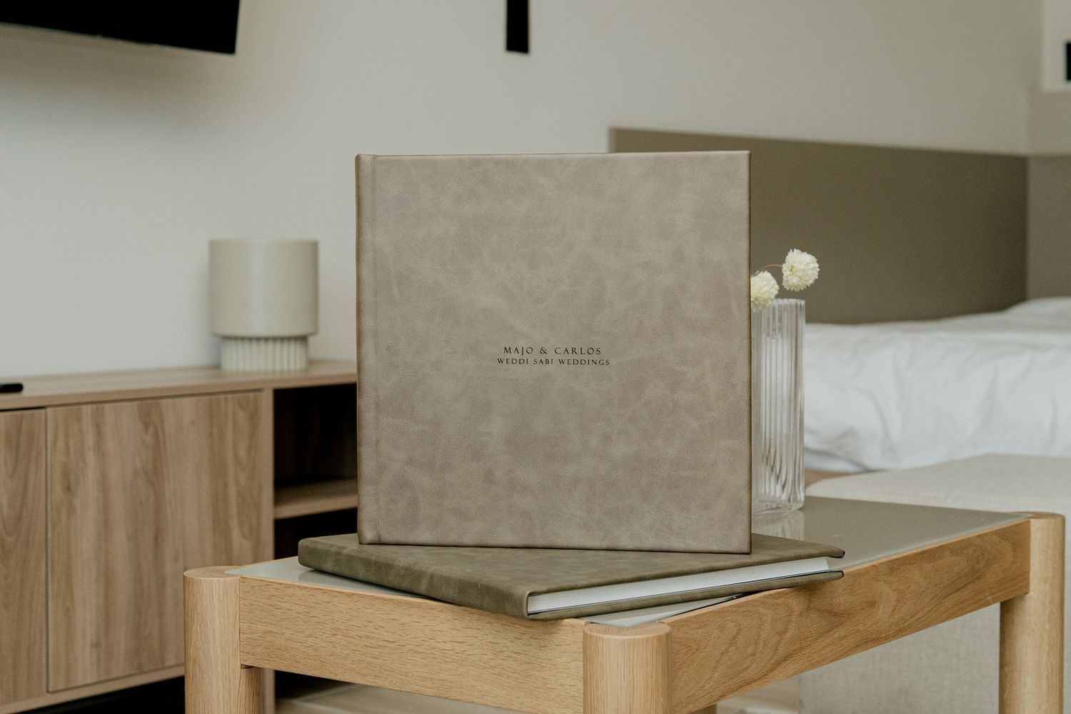 Elegant beige linen photo album box displayed on a wooden side table in a modern hotel room.