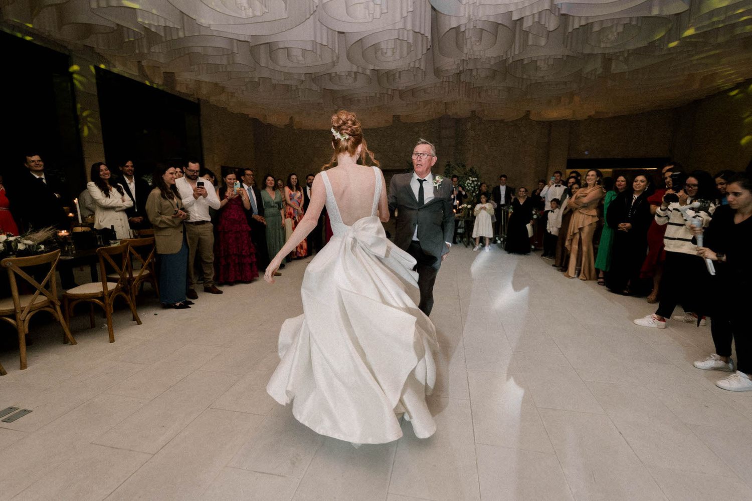 A couple dances at their wedding reception while guests watch from the sides of the dance floor.