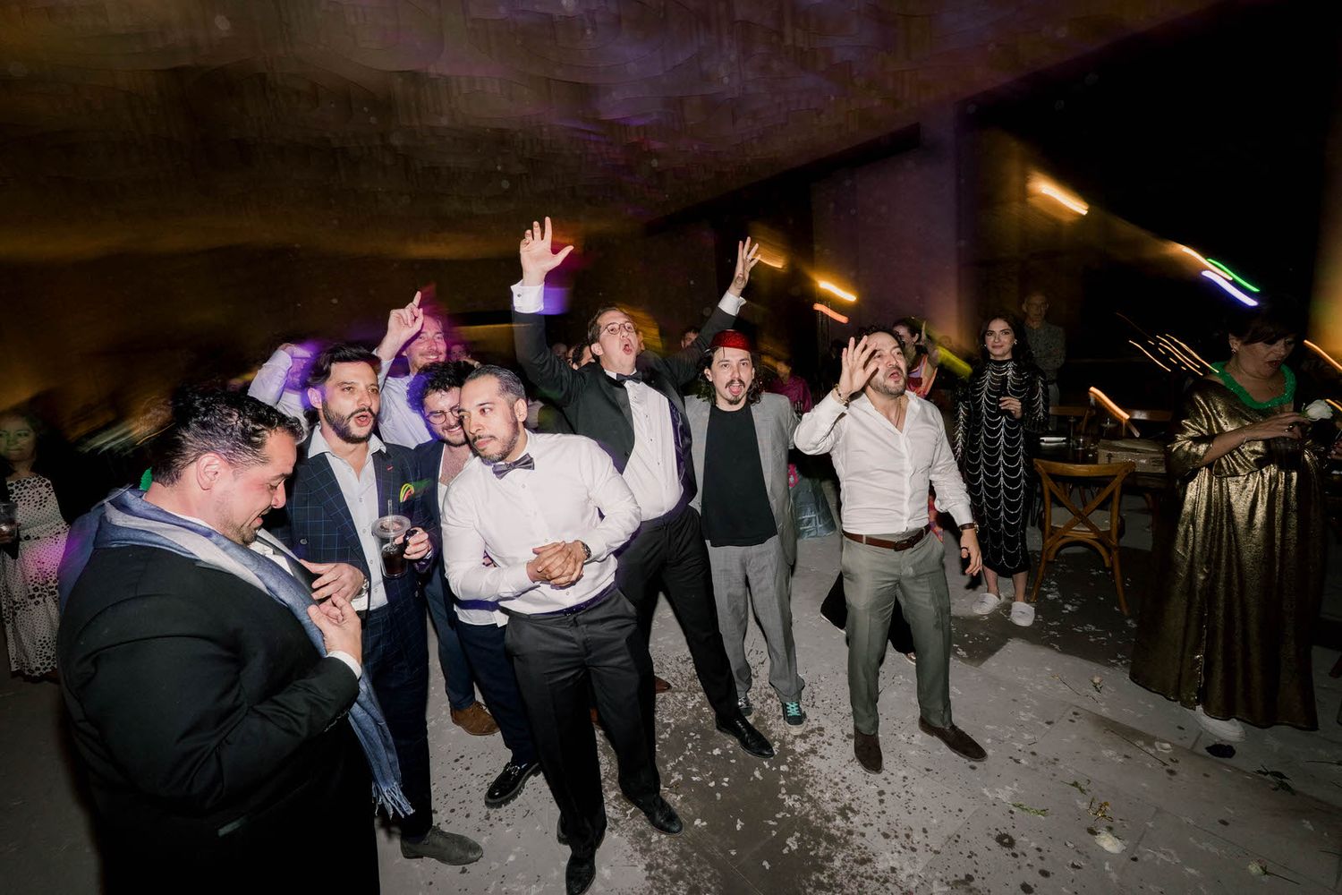 Wedding guests jump and dance together during a lively reception celebration.