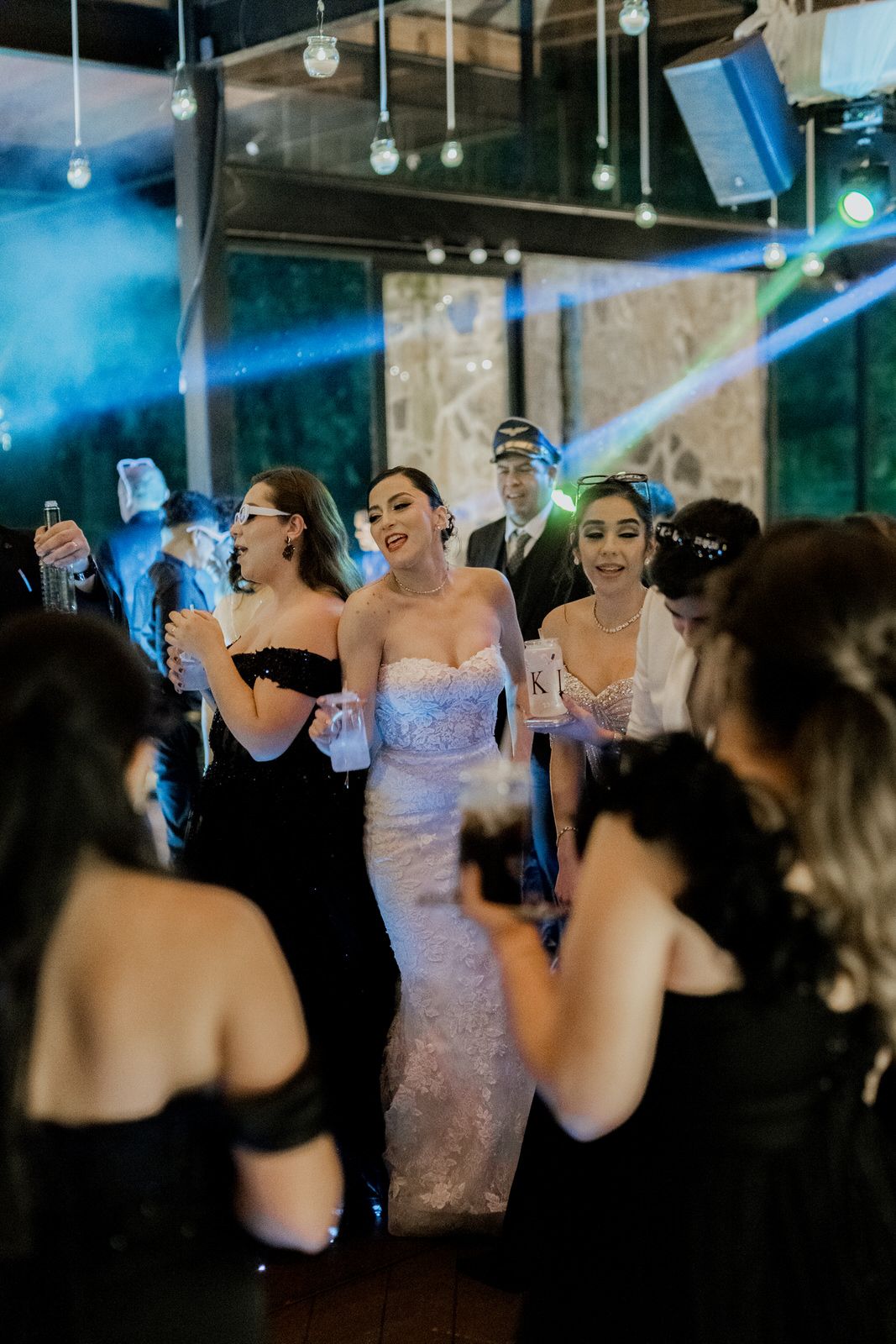 People dancing under blue lighting at an indoor celebration with hanging decorative lights.