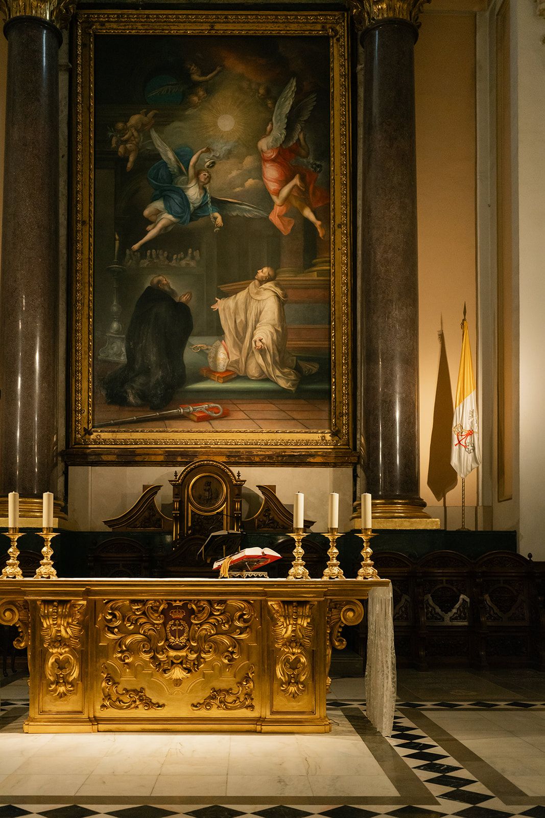 Ornate gold altar with candles and religious paintings in an elegant church interior.