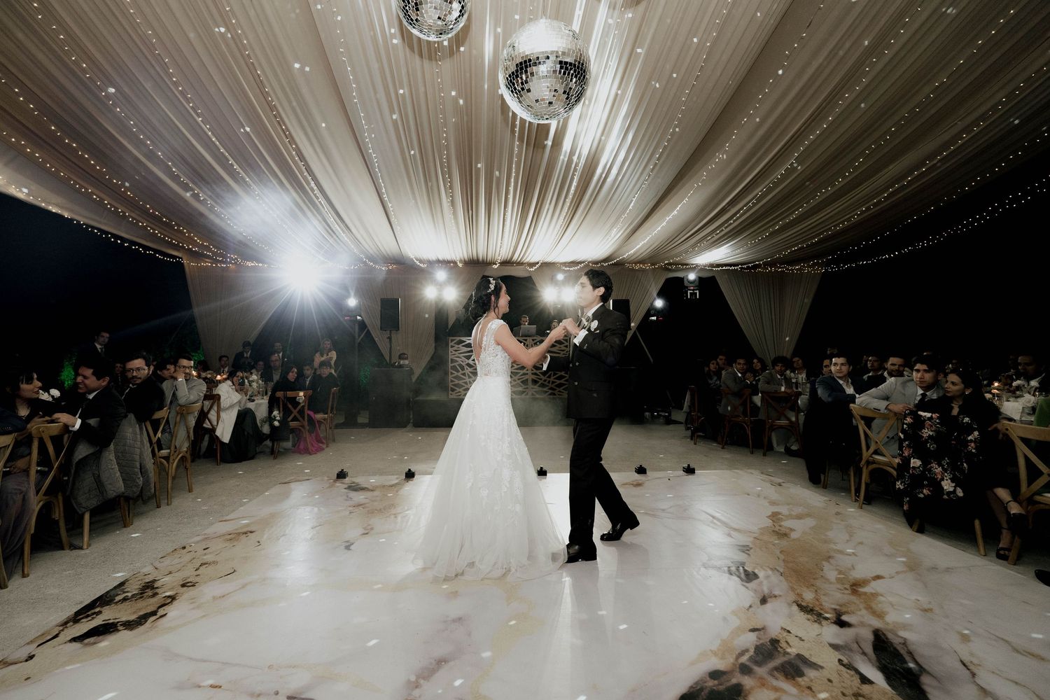 Elegant wedding venue with white fabric draped ceiling and sparkling disco ball illuminating the dance floor.