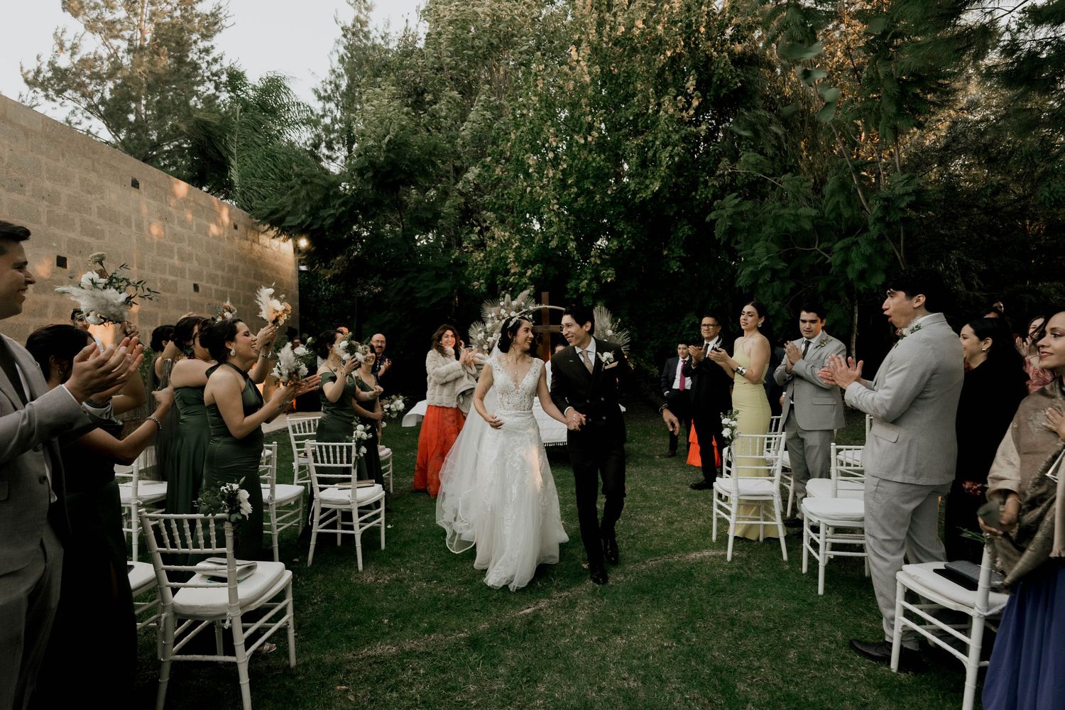Outdoor wedding celebration with white chairs and guests enjoying the garden atmosphere.