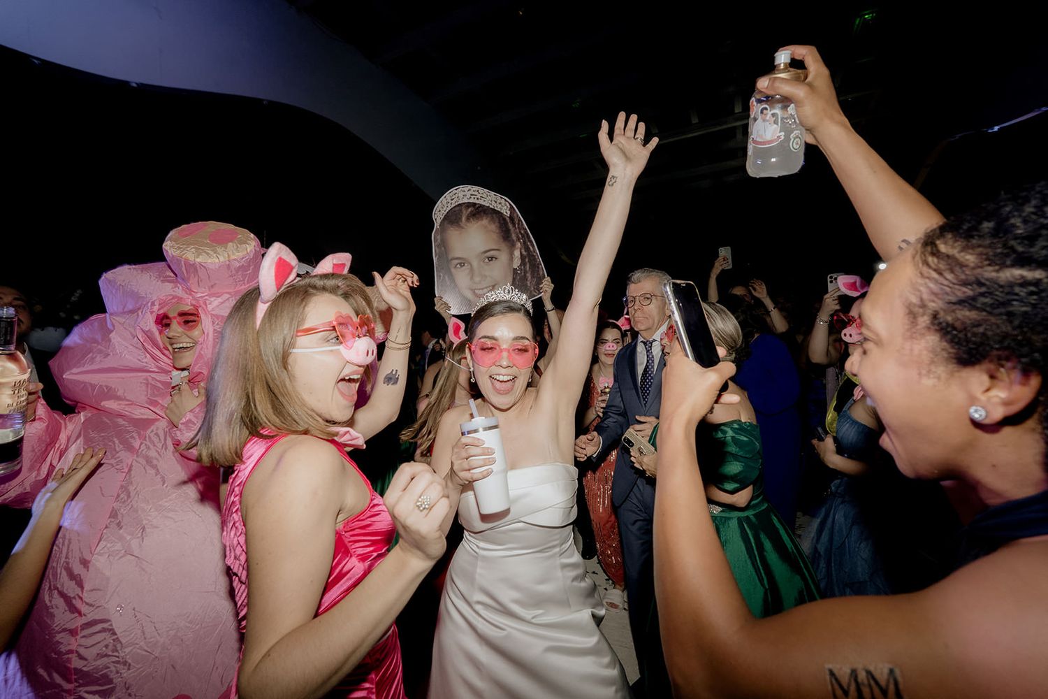 Bride and guests celebrating on dance floor wearing fun costumes and accessories at lively wedding party.